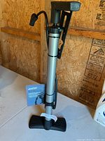 Full view of the CCM bicycle pump showing its silver metallic body, black foot base and handle, and flexible hose with valve adapter.