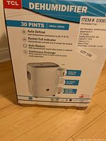 Photo of TCL brand dehumidifier box showing 30 pints capacity and key features such as auto defrost, bucket full indicator, auto restart, continuous drainage, built-in handle, up front bucket, casters for portability.