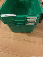 Stacked green plastic shopping baskets showing the label 'bin paid for!' on front of basket, with black handles and smooth plastic build.