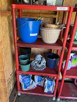 Red plastic shelving unit with four shelves, showing overall view including some garden pots and supplies (not included).
