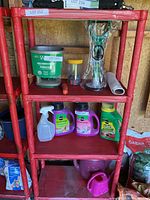 Red plastic shelving unit with various items stored on shelves including gardening and household products in a shed environment.