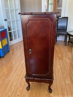 Front view of the closed standing jewelry case showing decorative front door and claw feet.