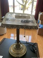 Front view showing the lamp on a table with frosted glass shade and metal base under natural light.