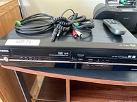 Full view of the Toshiba VHS DVD Video Cassette Recorder D-VR7 with cables and remote on top.