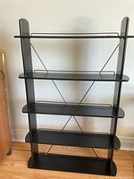 Front view of the black wood shelving unit showing four shelves and metal wire back supports