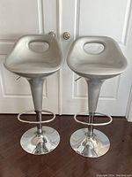 Two silver plastic and chrome adjustable bar stools shown front facing with pedestal bases and footrests.