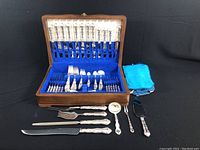 Open wooden case showing full flatware and serving set against black backdrop