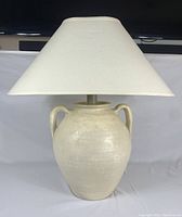 Full view of the ceramic table lamp showing the urn-shaped base and wide fabric shade.