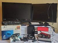 Full lot setup showing two monitors, boxed LG DVD rewriter, Sony FM/AM Walkman, red Sony Bluetooth speaker, Logitech headset, Samsung Blu-ray player, various cables and Xbox controller.