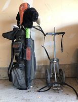 Photo showing full golf bag with clubs, umbrella, and vintage metal golf caddy beside it.