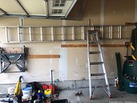 Garage wide view showing both ladders: extension ladder stored horizontally on wall hooks and stepladder standing.