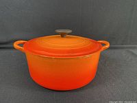 Closed view of orange Le Creuset Dutch oven with lid on, showing exterior and handles.