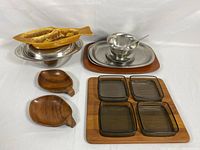 Overview photo showing all serving dishes including the stainless steel dish with lid, yellow fish-shaped ceramic dish, wood and steel dish, vintage platter with glass inserts, and wooden leaf-shaped small dishes.