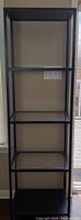Full front view of tall metal and glass shelving unit with five shelves.