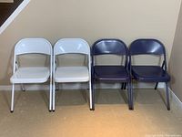 Four metal folding chairs, two white and two blue, front view showing seats and backrests