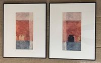 Two framed abstract prints side by side with predominantly red, blue and beige color blocks, each in dark brown frame with white matte board.