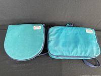 Two teal Pyrex Portables carrying cases, one round and one rectangular, displayed side by side on black surface