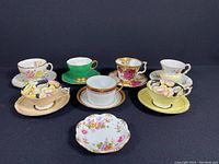 Group view of seven tea cup and saucer sets plus trinket dish on black background