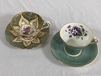 Two tea cups and saucers displayed side by side, showing front and overall design of Paragon and Aynsley Corset cups.