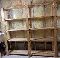 Front view of the wooden shelving unit in an unfinished basement with four shelves and visible metal cross bracing at the back.