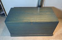 Top front view of closed green wooden storage box with visible keyhole on front panel.