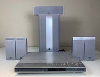 Front view showing Yamaha DVD home theatre player with buttons and volume dial and speakers including large subwoofer, center, and four satellite speakers arranged behind.
