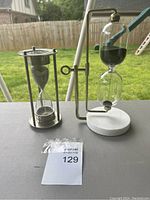 Two glass hourglasses placed on a flat surface outdoors, showing overall view of both items.