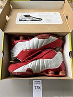 Side view of left and right Nike Shox basketball shoes in red and silver color inside open box.