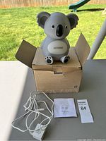 Koala-shaped diffuser sitting on open box outdoors with power cord and instruction manual near it.