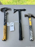 Three hammers on a gray surface, two claw hammers and a black Stanley slating hammer in the center