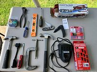 Photo showing variety of hand tools including hammers, clamps, spirit level, screwdrivers, pliers, utility knives, Dremel rotary tool, drill bit cases and accessories such as oil bottle and plug adapter.