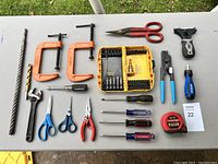 Top-down view showing all tools arranged on a white table: scissors, clamps, clamp, pliers, wrenches, multiple screwdrivers, bit set, tape measure.