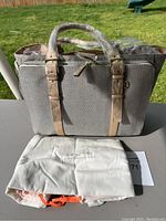 Front view of beige canvas tote bag with leather straps and dust cover.
