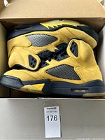 Side view of the pair of Air Jordan 5 Retro sneakers showing yellow nubuck and mesh upper, black midsole, and outsole in box.