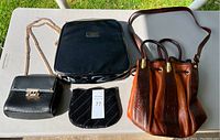 Full view of all four bags on table: black Lancome makeup bag, brown leather purse, black change bag, and black Luana purse with gold chain strap