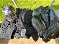Photo showing the full lot of motorcycle gear including helmet, protective vest, and leather jacket on a white table outdoors.