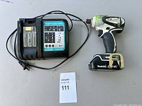 Makita cordless drill with attached battery and charger on surface with lot number card