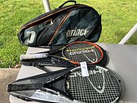 Prince tennis bag, two tennis rackets and two black racket covers displayed on table outdoors.