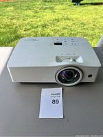 Front view of white Optoma projector on table with control buttons on top and lens visible in front.