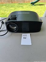 Side view of the black Goodisbe projector showing lens and power cable.