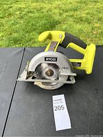 Front view of the Ryobi cordless circular saw placed on a black surface showing yellow handle, silver blade guard with 18V marking and Ryobi logo on blade cover.