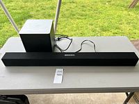 Black Vizio soundbar placed in front of black subwoofer on white table against outdoor grass background.