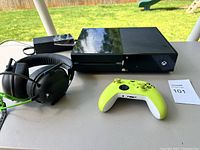 Xbox One console, yellow-green controller, headset with microphone, and power supply on table outdoors