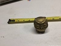 Small brass owl figurine shown next to measuring tape indicating approximately 2.5 inches tall.