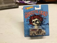 Image showing an unopened Hot Wheels Grateful Dead Dairy Delivery diecast car in original packaging with blue background and skull with roses artwork.