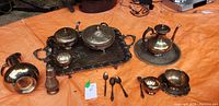 Overview of assorted copper and brass items on orange surface, showing tray, utensils, covered bowl, teapot, and other items.