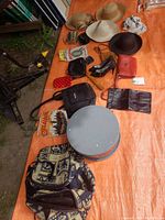 Photo showing multiple hats, handbags, wallets, and small accessories arranged on an orange tarp outdoors.