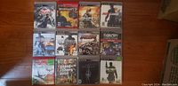 Photo showing 14 PlayStation 3 game cases laid out in rows on a wooden floor, titles visible include Dead Space 2, Resistance 2, Sniper, Just Cause 2, Battlefield, Far Cry compilation, GTA IV, Skyrim, Call of Duty MW3