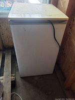 Photo of the closed small white bar fridge showing overall condition and crack on top