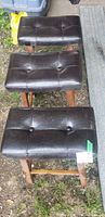 Top-down view of the three matching bar stools showing their brown tufted faux leather seats with button details and wooden legs.